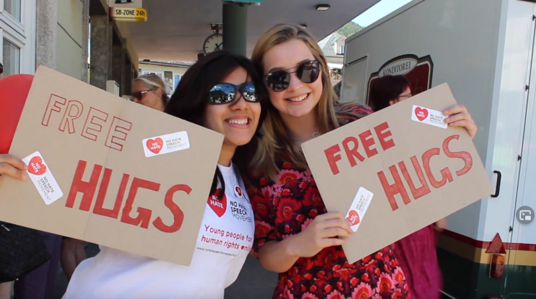 Das Bild zeigt zwei lachende Mädchen, die Free-Hugs Schilder in den Händen halten.