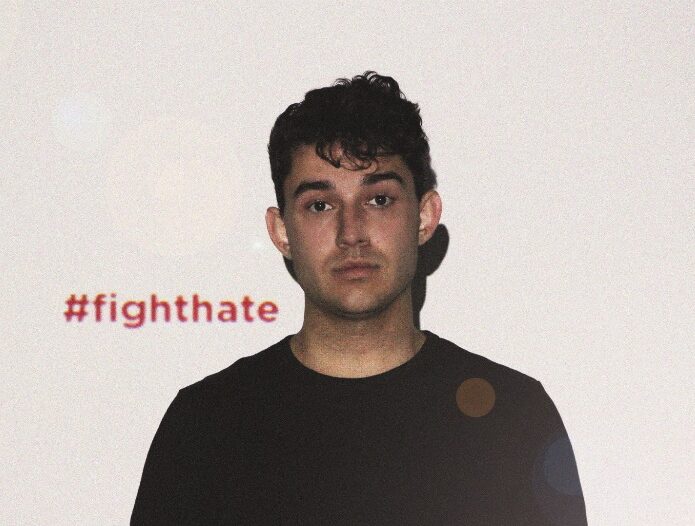 Ein Mann mit kurzen Braunen Haaren schaut vor einer weißen Wand direkt in die Kamera. Links daneben steht #fighthate