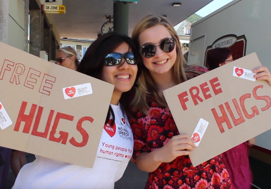 Das Bild von zwei Frauen mit Sonnenbrille, die jeweils ein Schild aus Karton halten mit den Worten "Free Hugs"